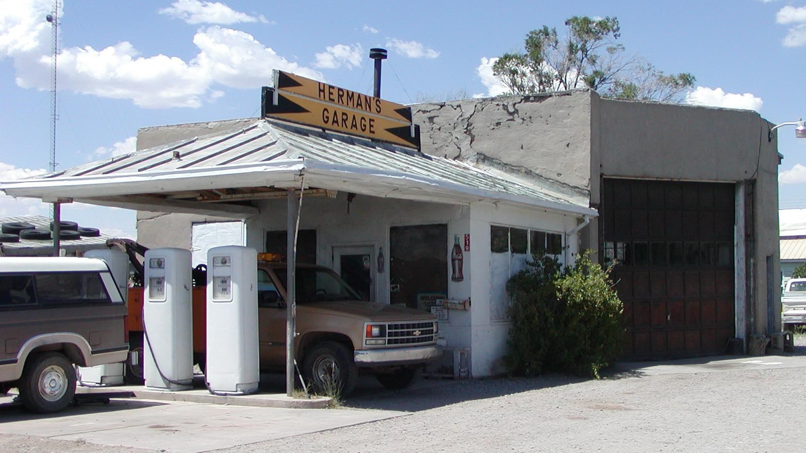 A grey stucco building with an extended patio and car. A yellow sign reads 