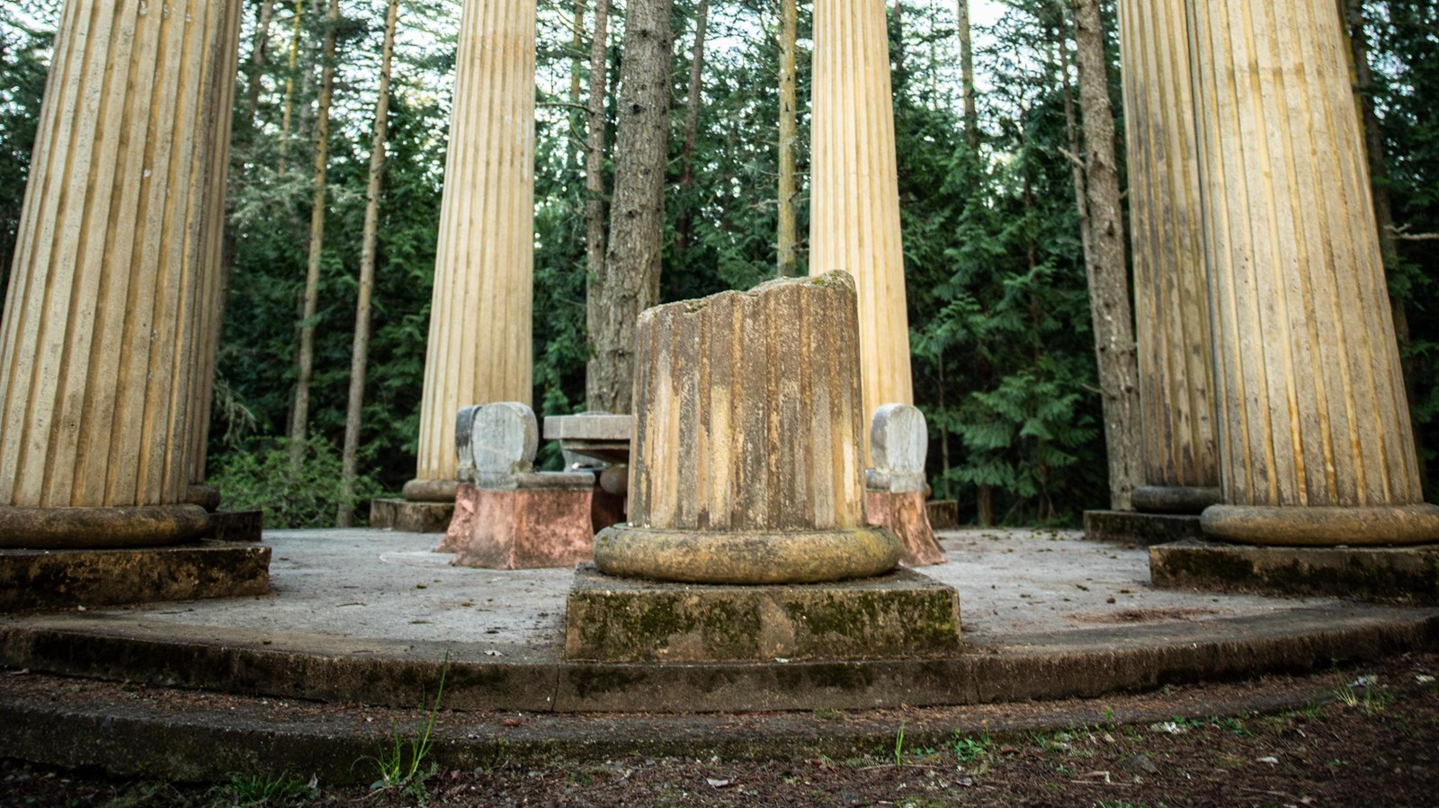 A monumental open air structure constructed of limestone and marble surrounded by woods