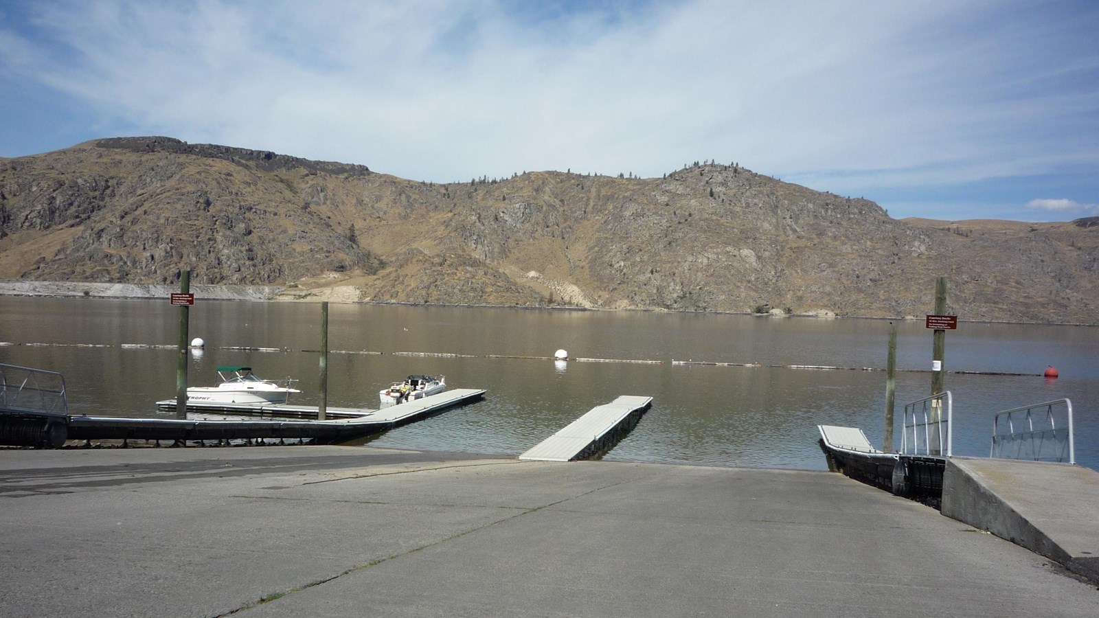 A view of the paved boat ramp with adjacent docks. An arc of log booms and buoys are visible beyond.