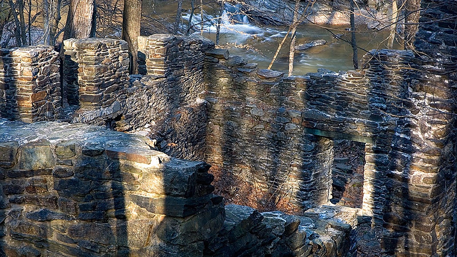 Photograph of stone walls of ruins with Sope Creek and the woods in the background.
