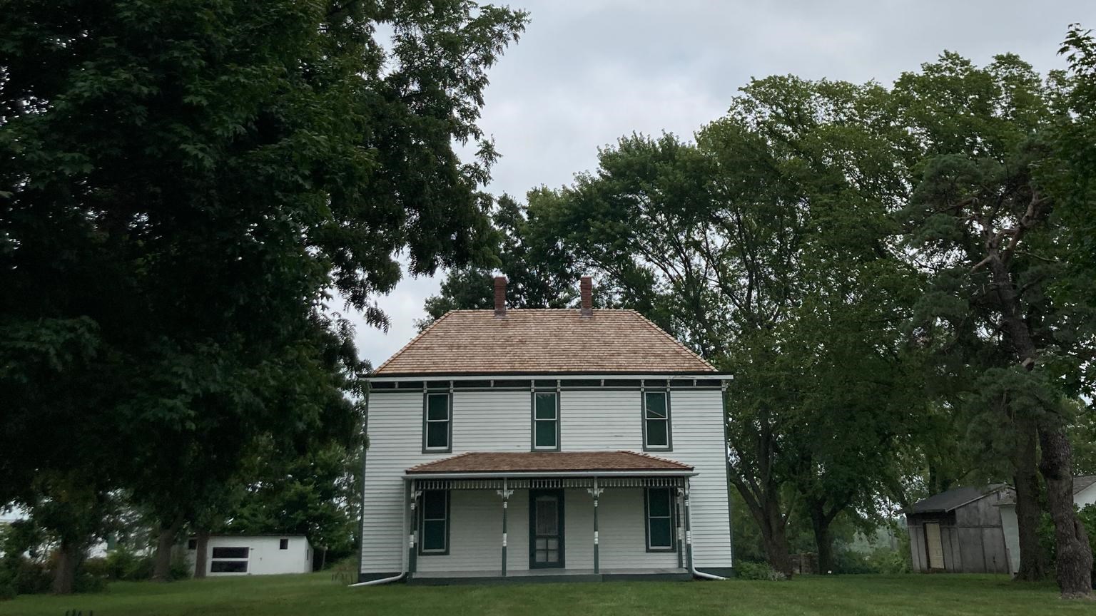 Tree canopy in the foreground, the two-story white Truman farm home in the background.
