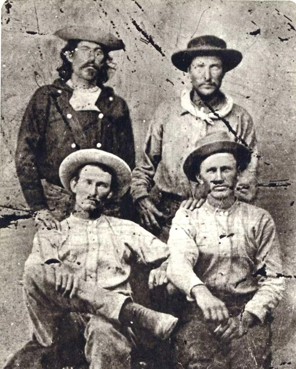 Historic image of four men sitting for a portrait wearing western American 1860s era clothing.