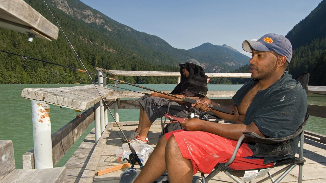 Two men sit fishing in chairs on a wooden pier