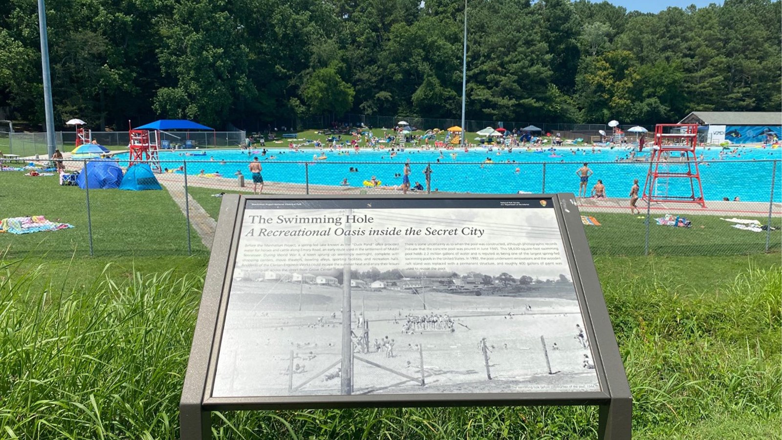 A wayside exhibit in the foreground of a large public pool.