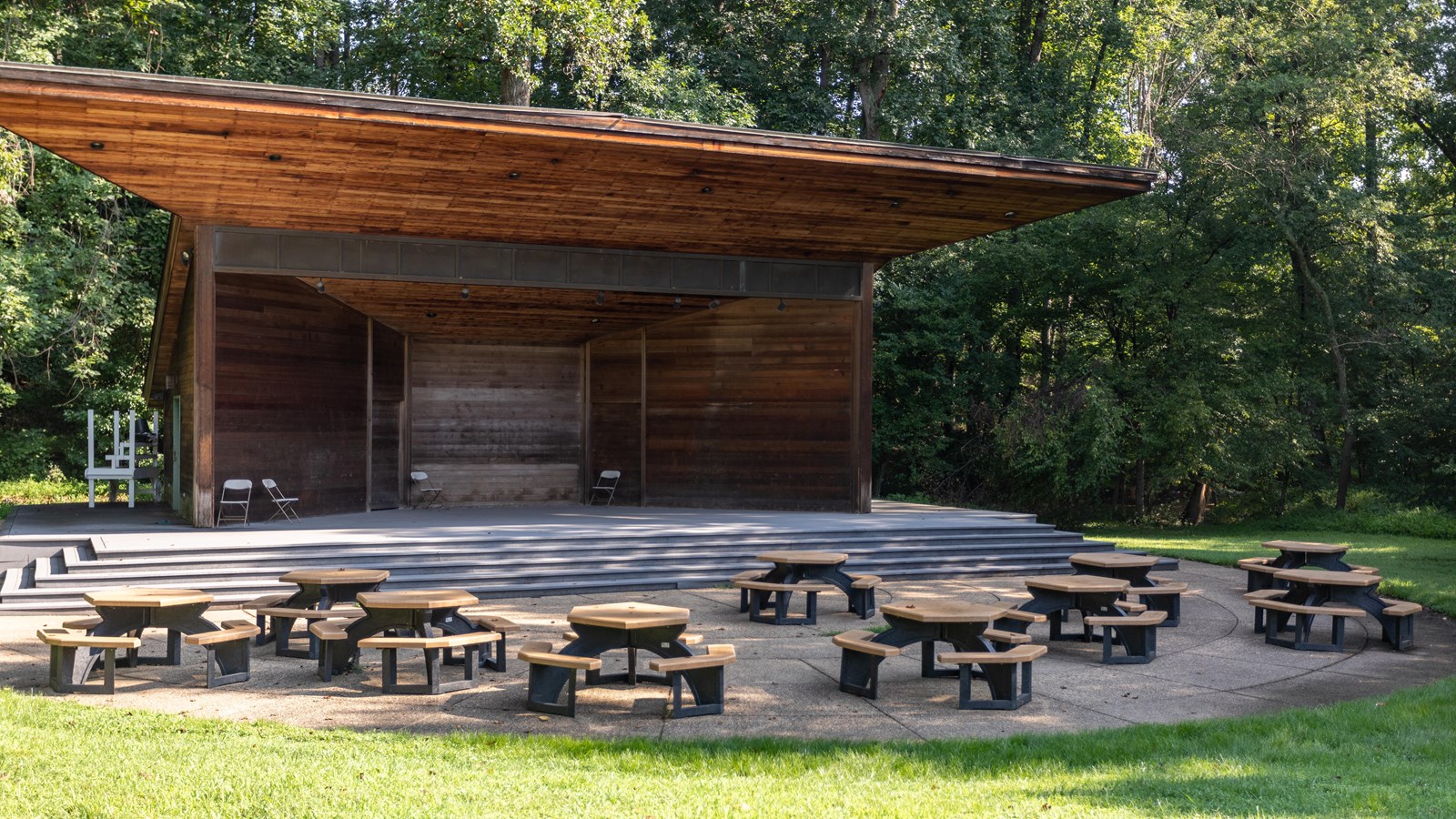 Stage with multiple steps coming from a concrete pad in front with picnic tables.