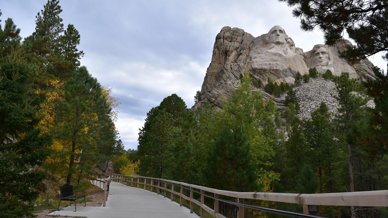 Concrete walkway with trees and Mount Rushmore National Memorial in the background.