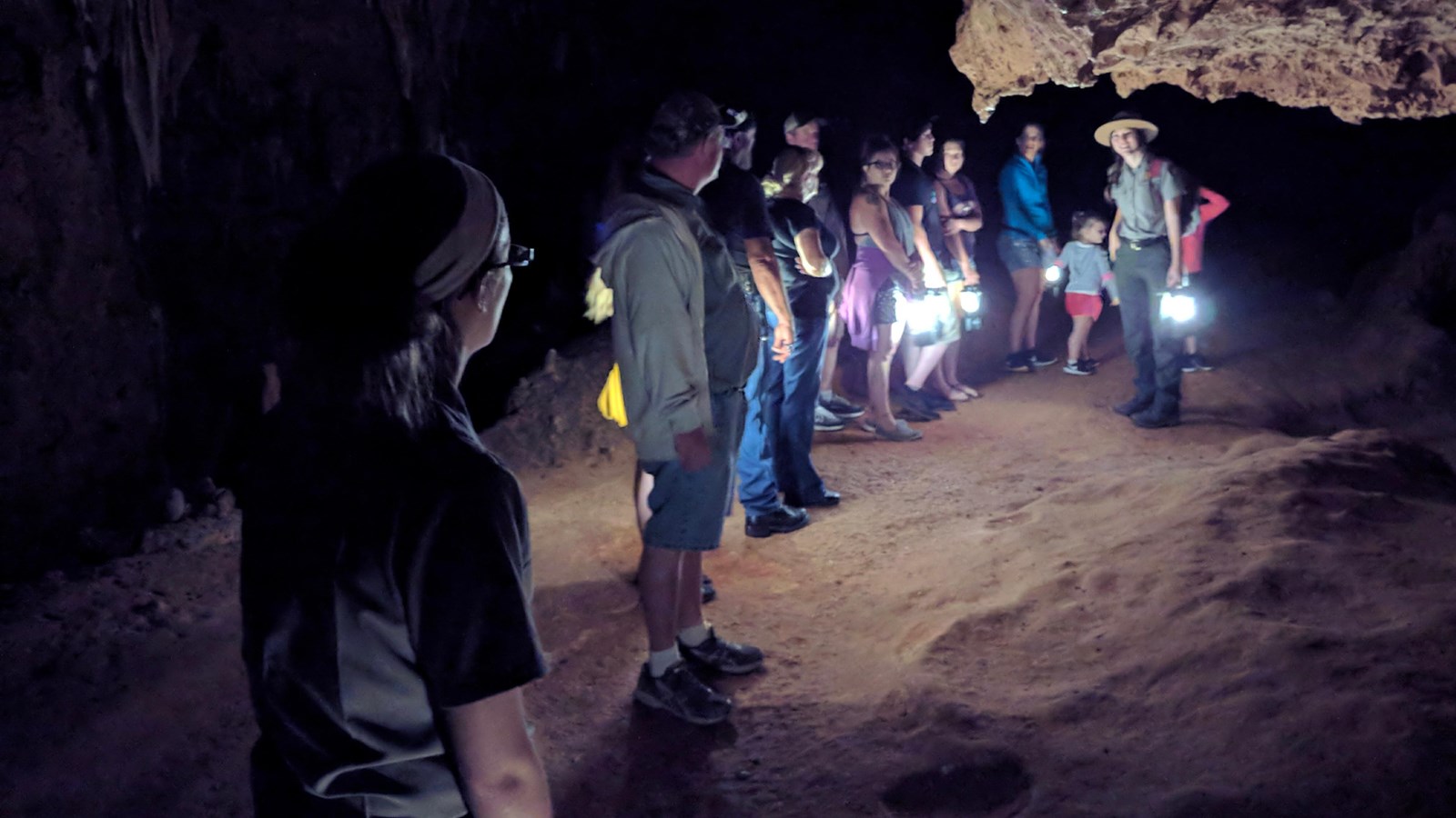 A group of people in the dark with lanterns during a cave tour, ranger and formations are visible.