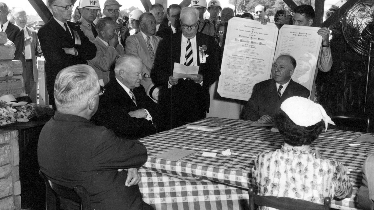 A 1950s photo depicts dignitaries honoring a distinguished old man at a picnic shelter.