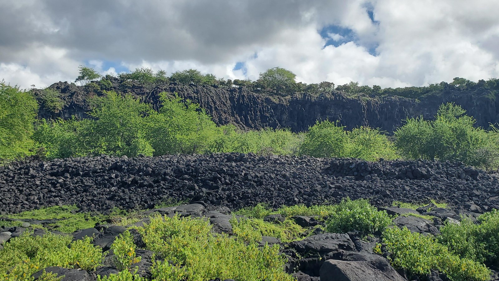 A large pile of stone rubble marks the ruins of the Alahaka Heiau with volcanic cliffs behind