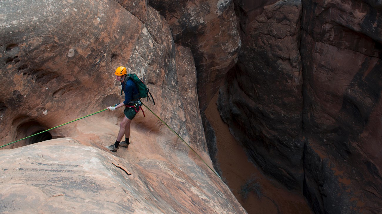 A person harnessed to a rope prepares to rappel into a canyon