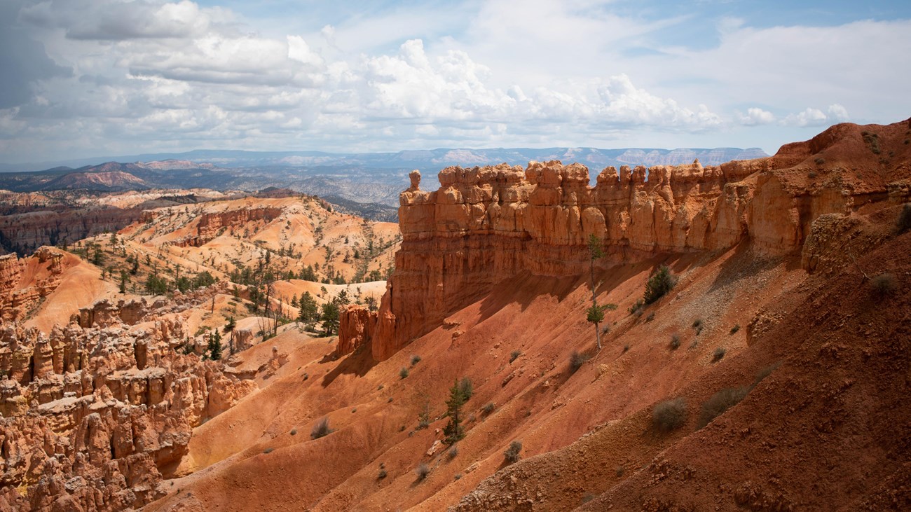 Red rock formations on top of a steep sandy slope with distant red rock formations in the background