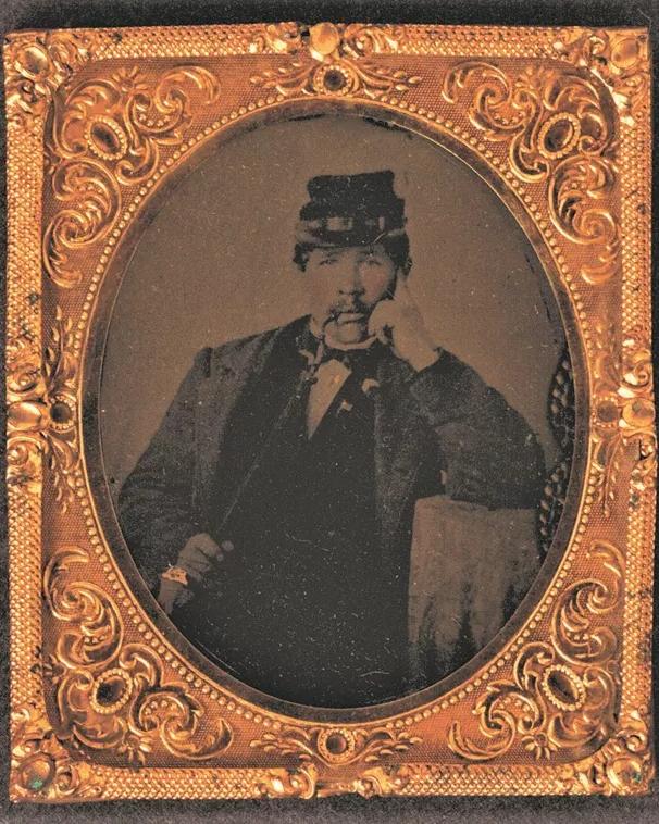 Black and white tin type photo of man in hat with pipe in gold frame