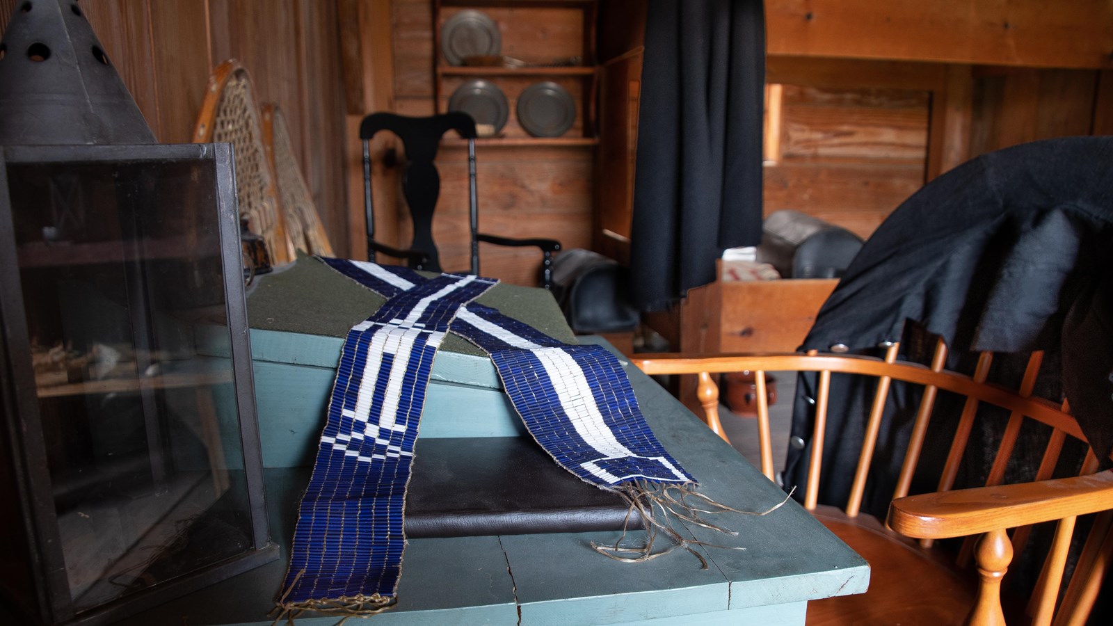 A table with beaded belts. A black jacket hangs on the back of a wooden chair.
