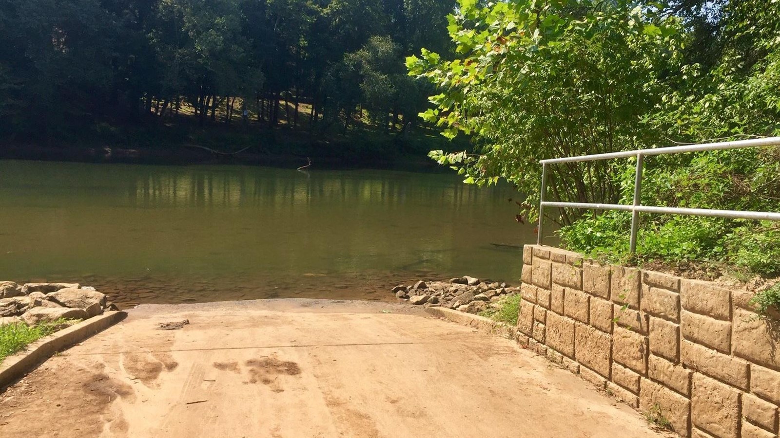 Ramp with wall and railing to the right, river in the middle and opposite wooded shoreline.