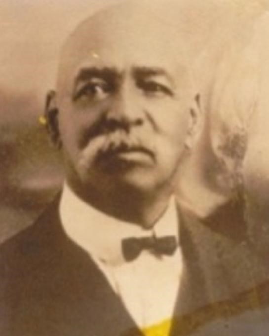 black and white picture of bald black man with which mustache and wearing bow tie and suit