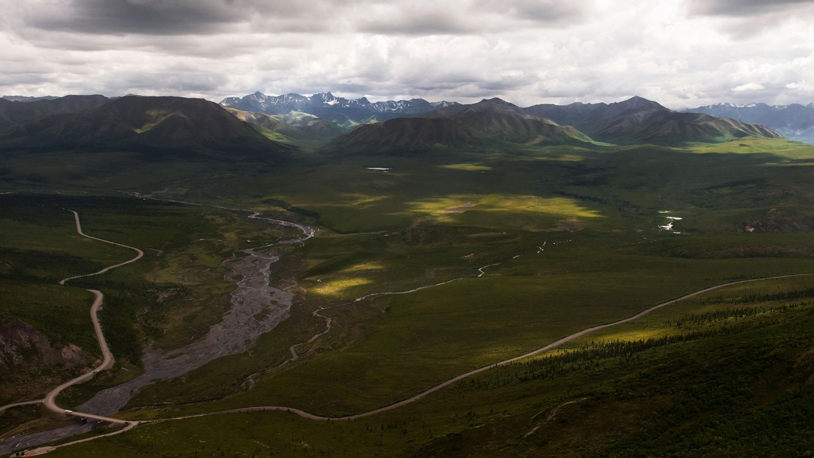 River and road with mountains in the background and a cloudy sky.