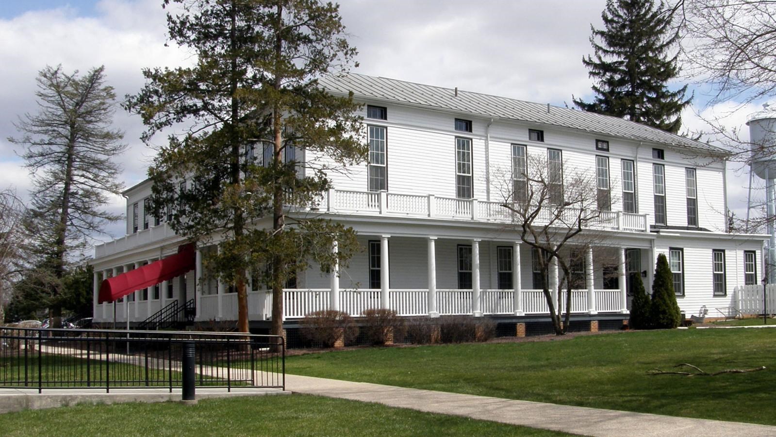 A two-story white building with a columned porch that wraps around most of the building.