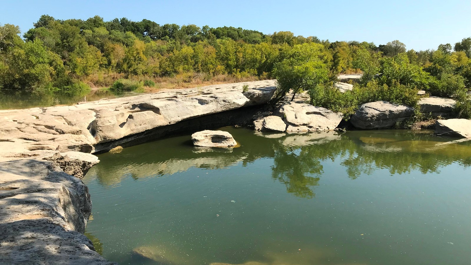 A rocky, smooth ledge, over a large pool of calm water. 