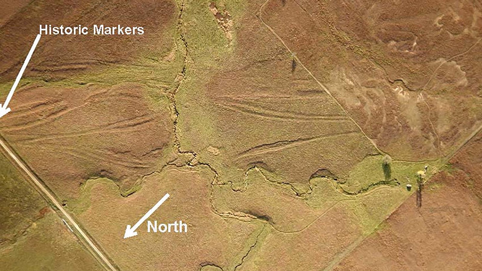 An aerial view of a large grassy field with visible trail ruts running north to south.