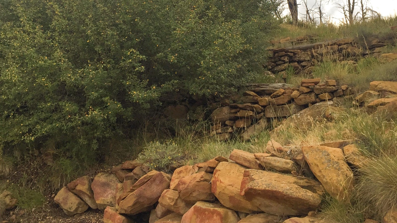 Three short, stone-masonry walls built one above the other along a steep slope.