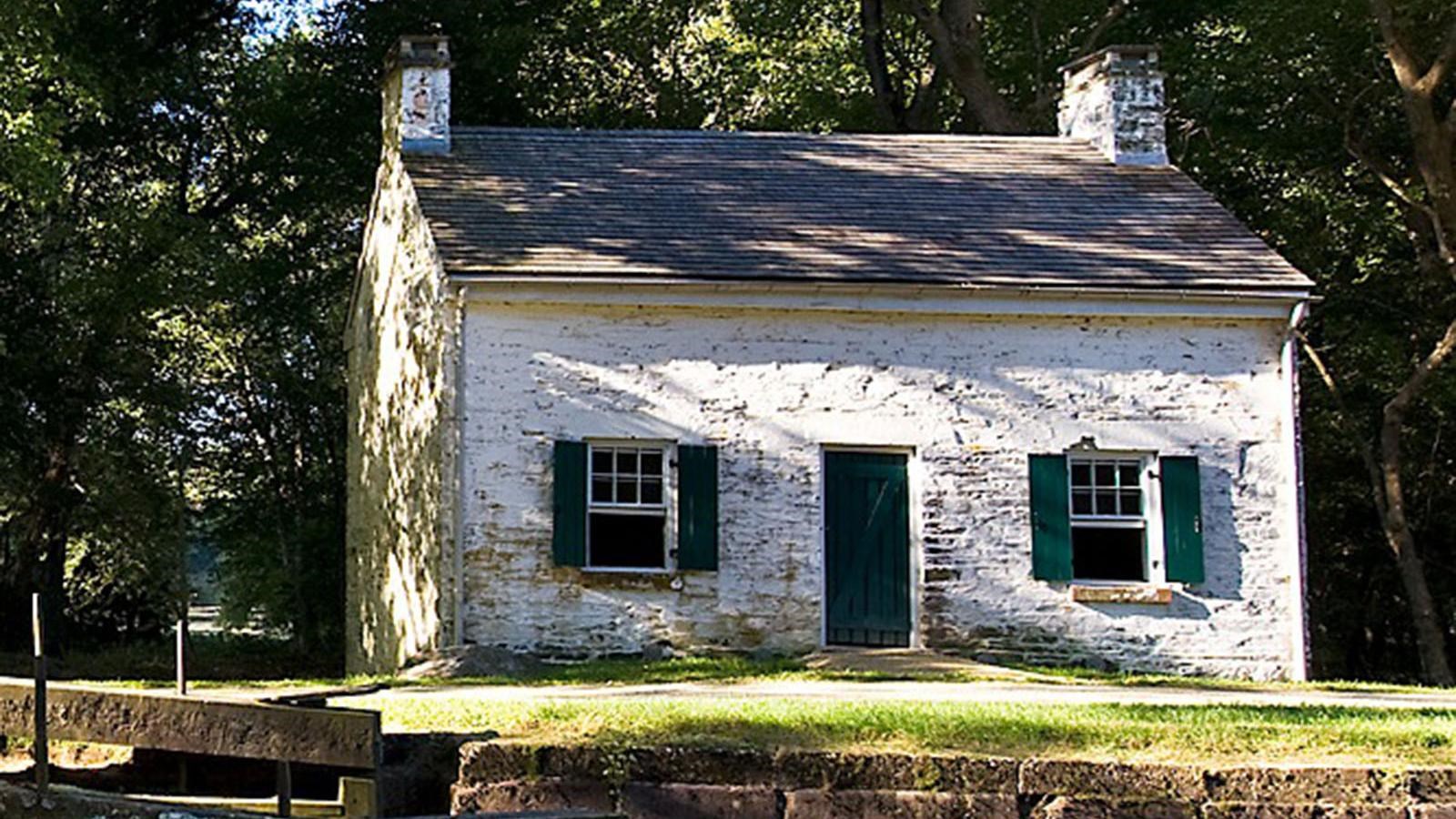 A lockhouse with a rectangular base and an A line roof sits on a patch of grass.