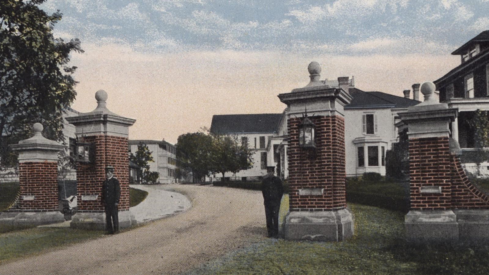 Two soldiers stand guard in front of brick gateposts that rise at least twice the size of a man.