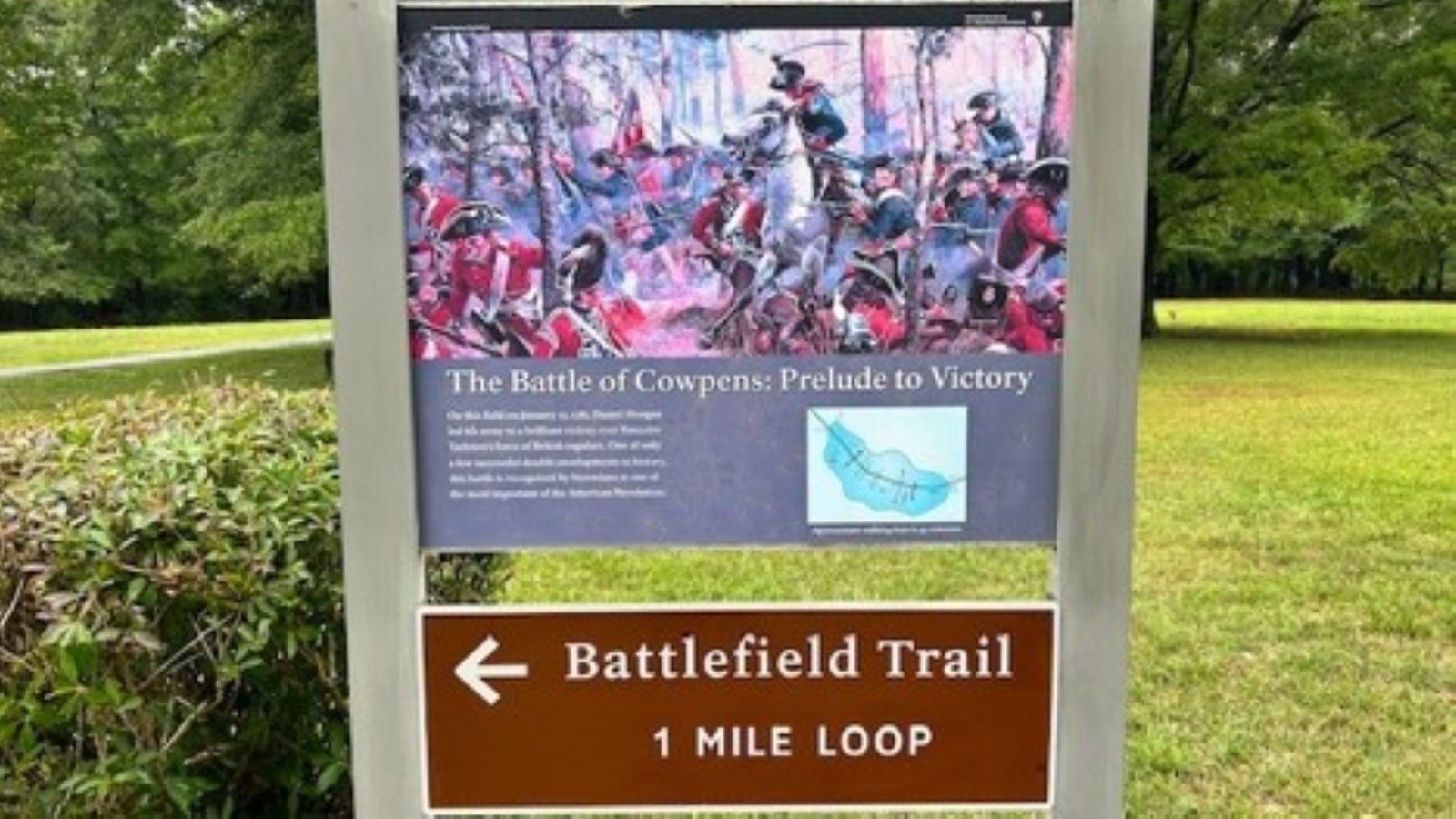 A wayside with a painting of soldiers and words in small font with a battlefield arrow left.