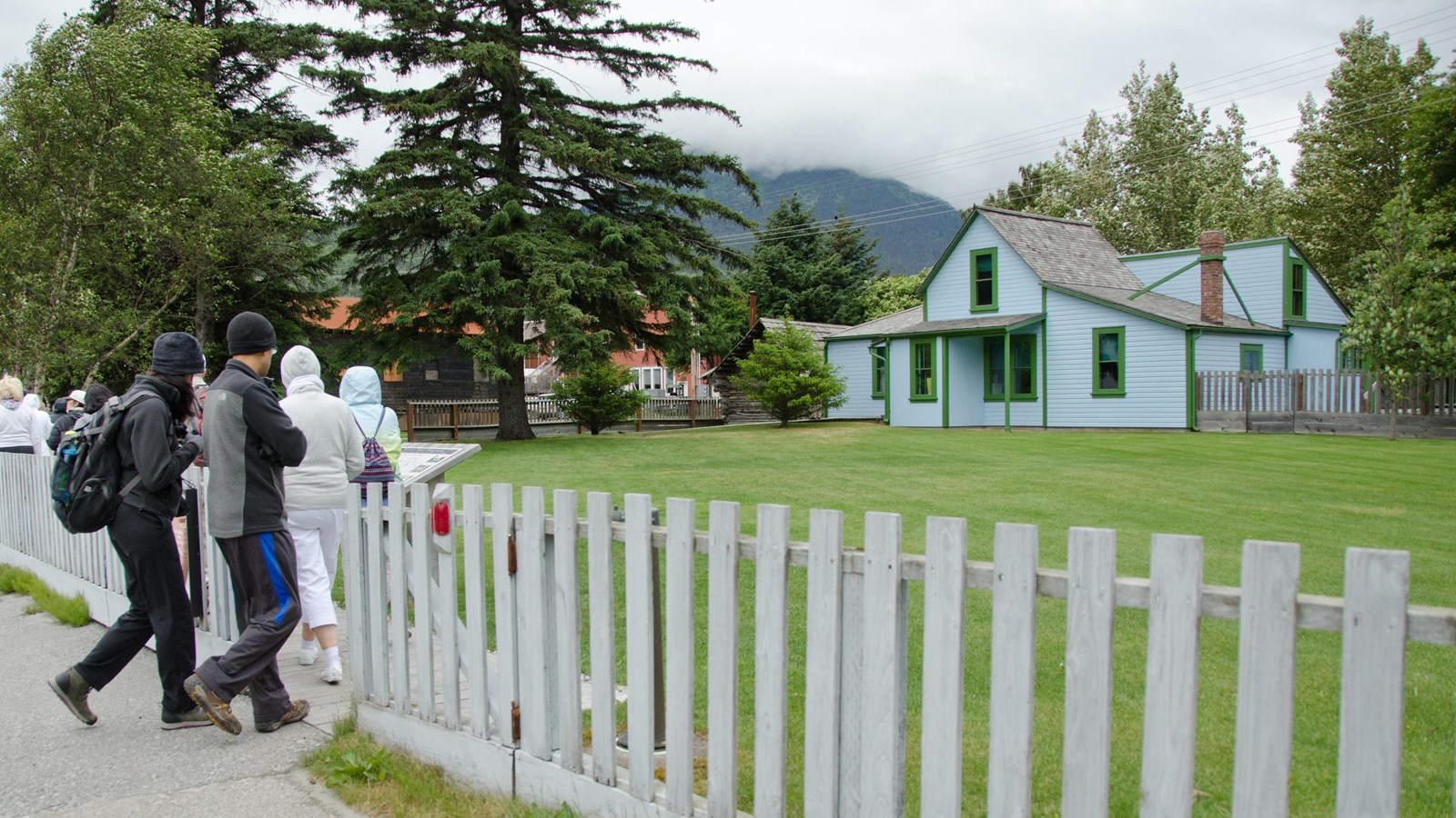 people walk through a fence to a grassy lawn and blue house