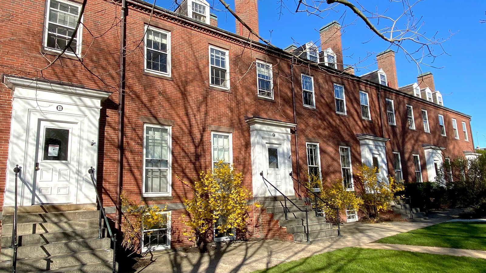 5 Federalist style brick townhouses with staircases leading up to each unit\'s white door.