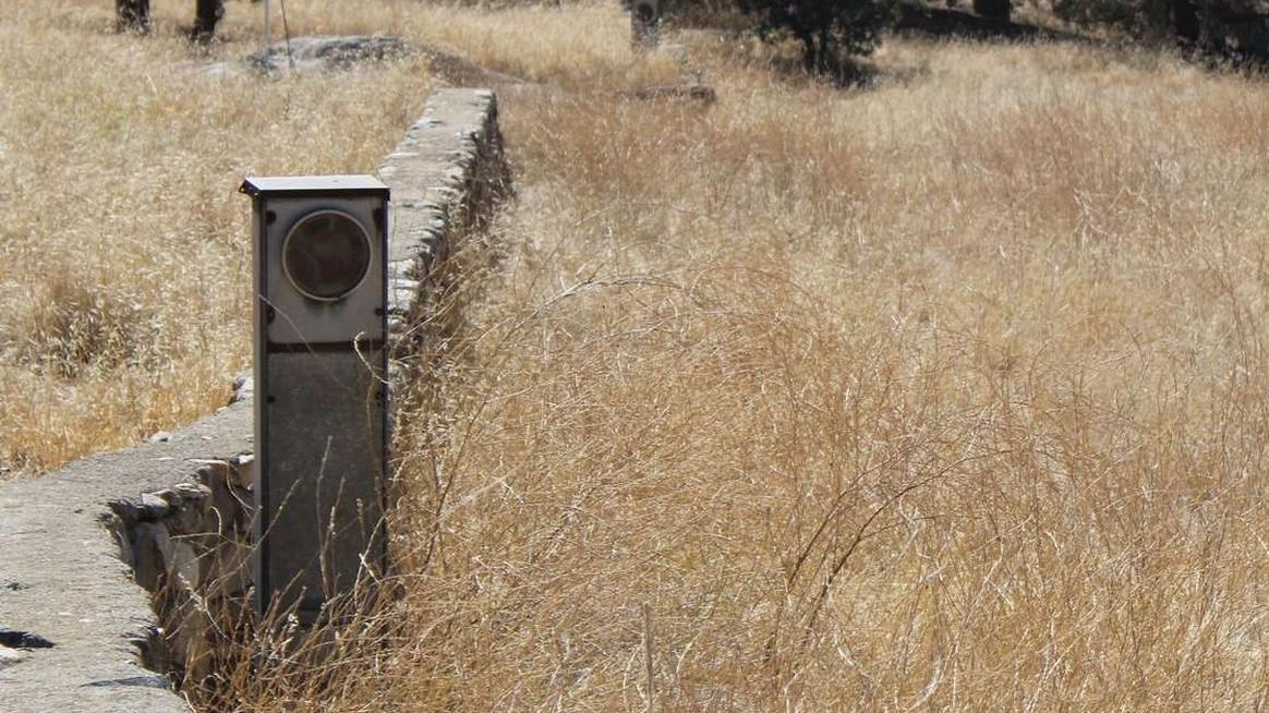 A small pedestal stands out from dry grasses near a low rock wall.