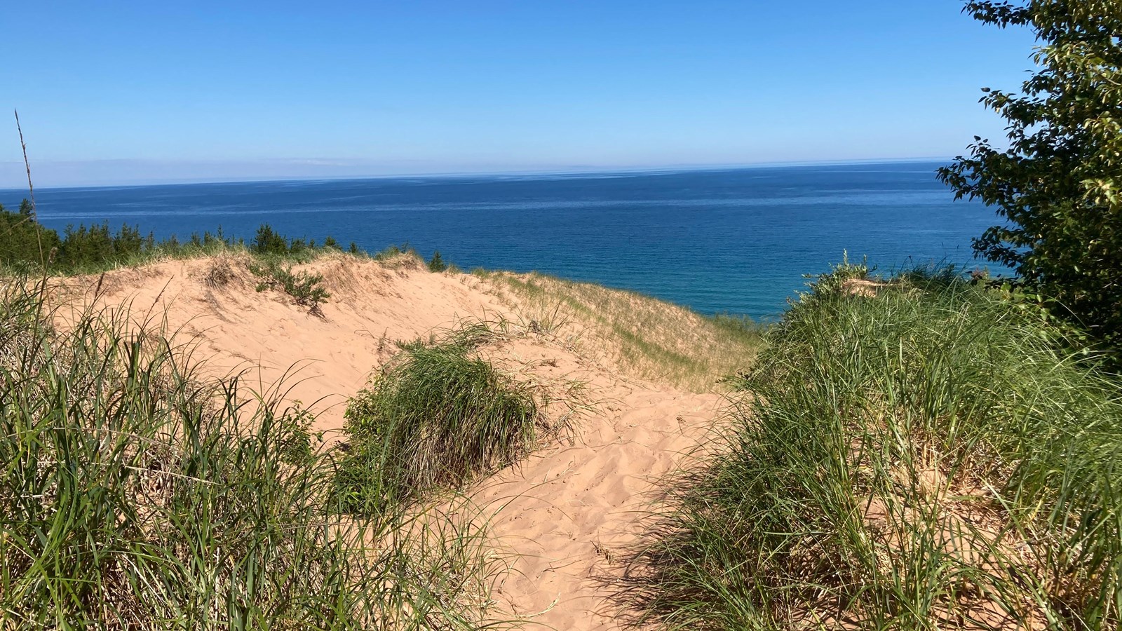 A trail through grass-covered sand dunes leads to a view of Lake Superior in the distance.