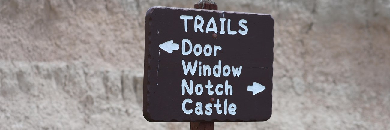 a brown sign with white writing points to door, window, notch, and castle trails.