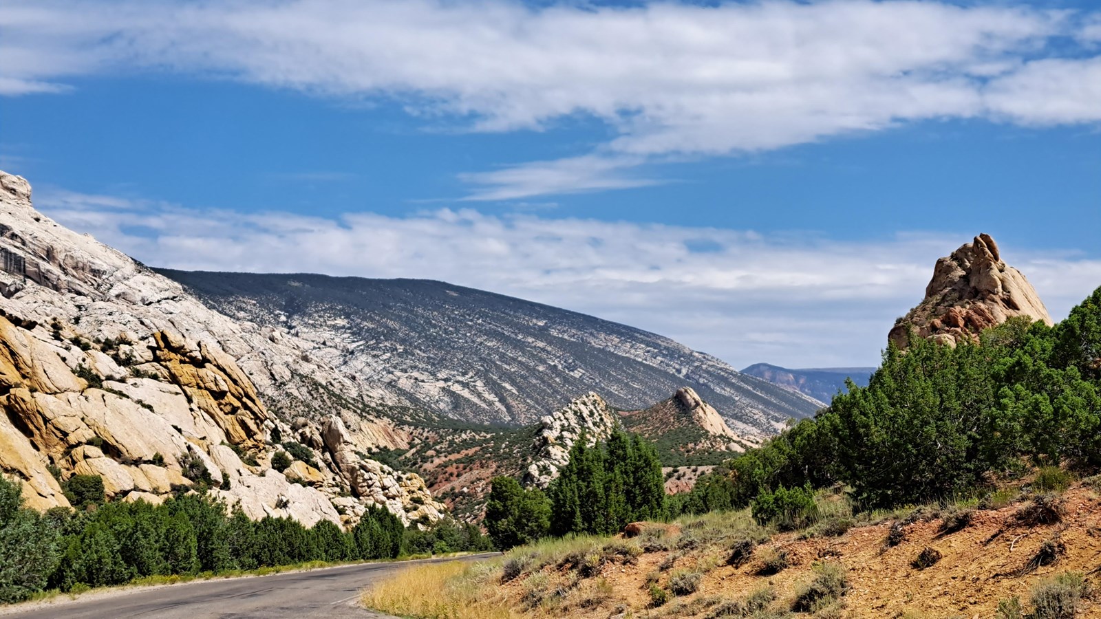 A roadside pullout looking downhill towards a large mountain surrounded by desert rock formations.
