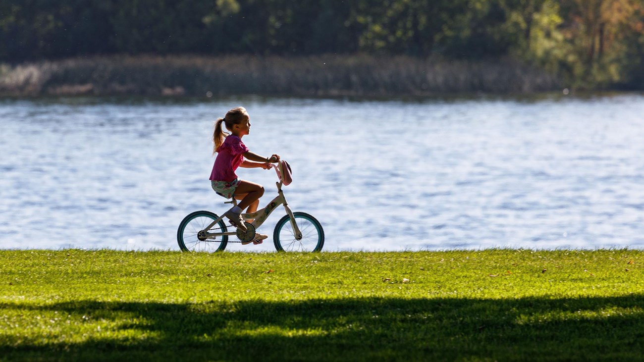 A young girl rides her bike in a grassy area along the river.