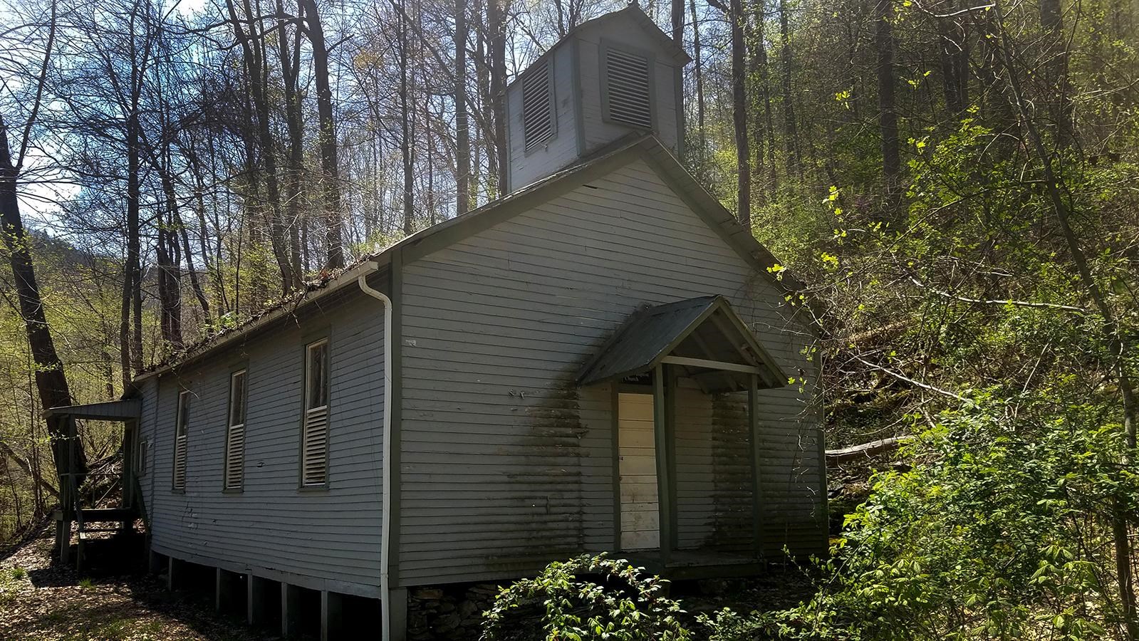 A blue sided church surrounded by the forest. 