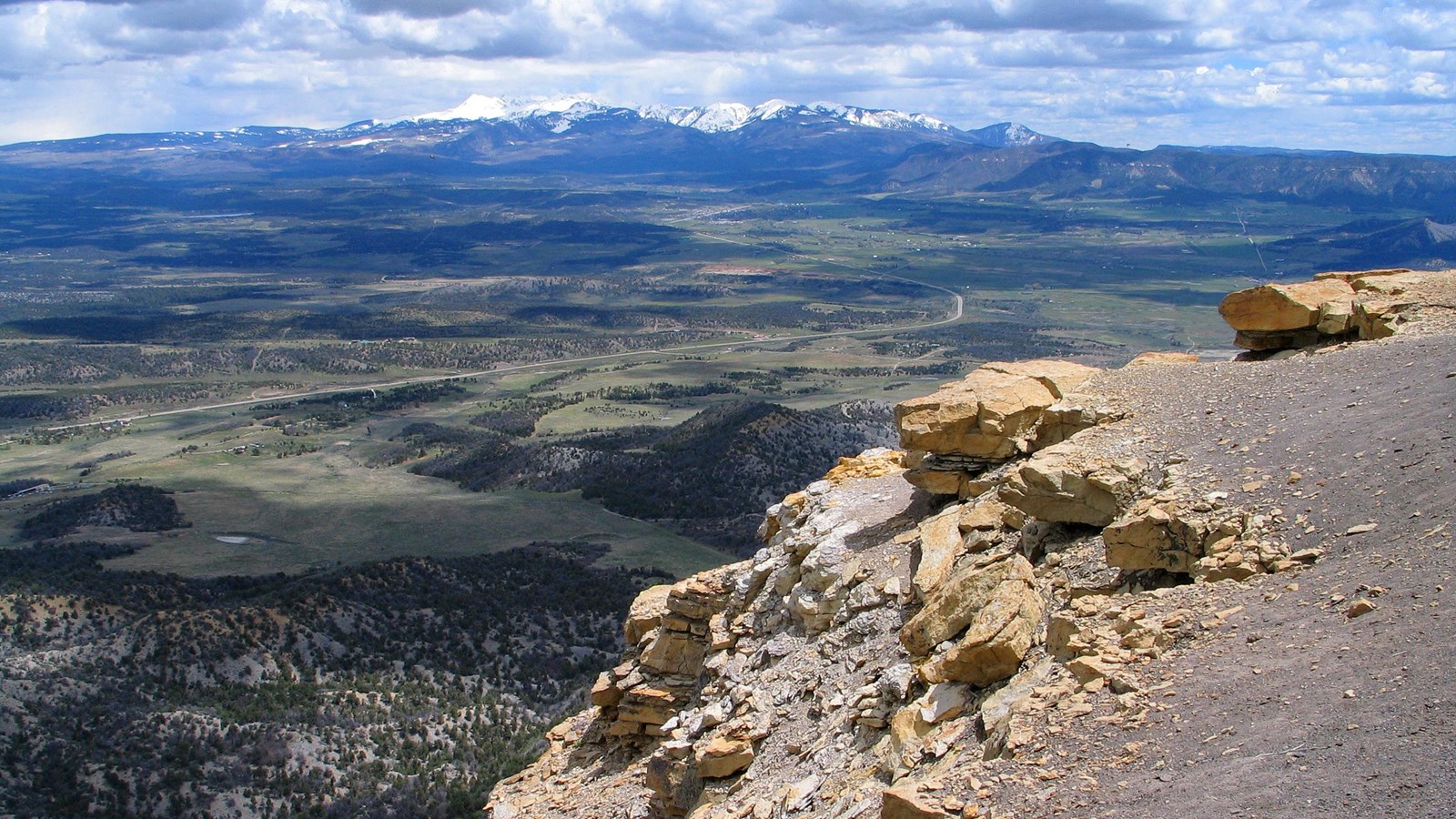 Overlooking a broad green valley with snow-capped mountains in the distance.