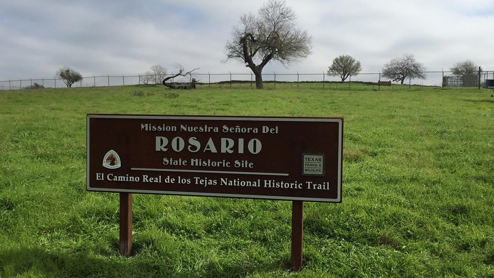 A large brown entry sign in a green, lush grass field.