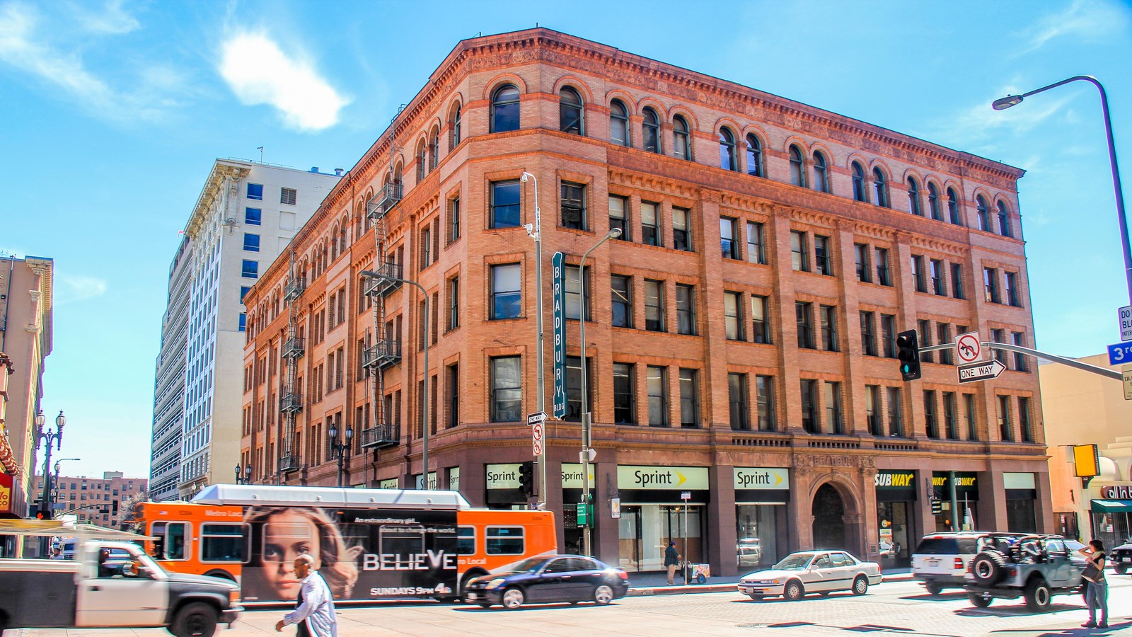 A brown multi-story building stands on the corner of a busy city intersection.