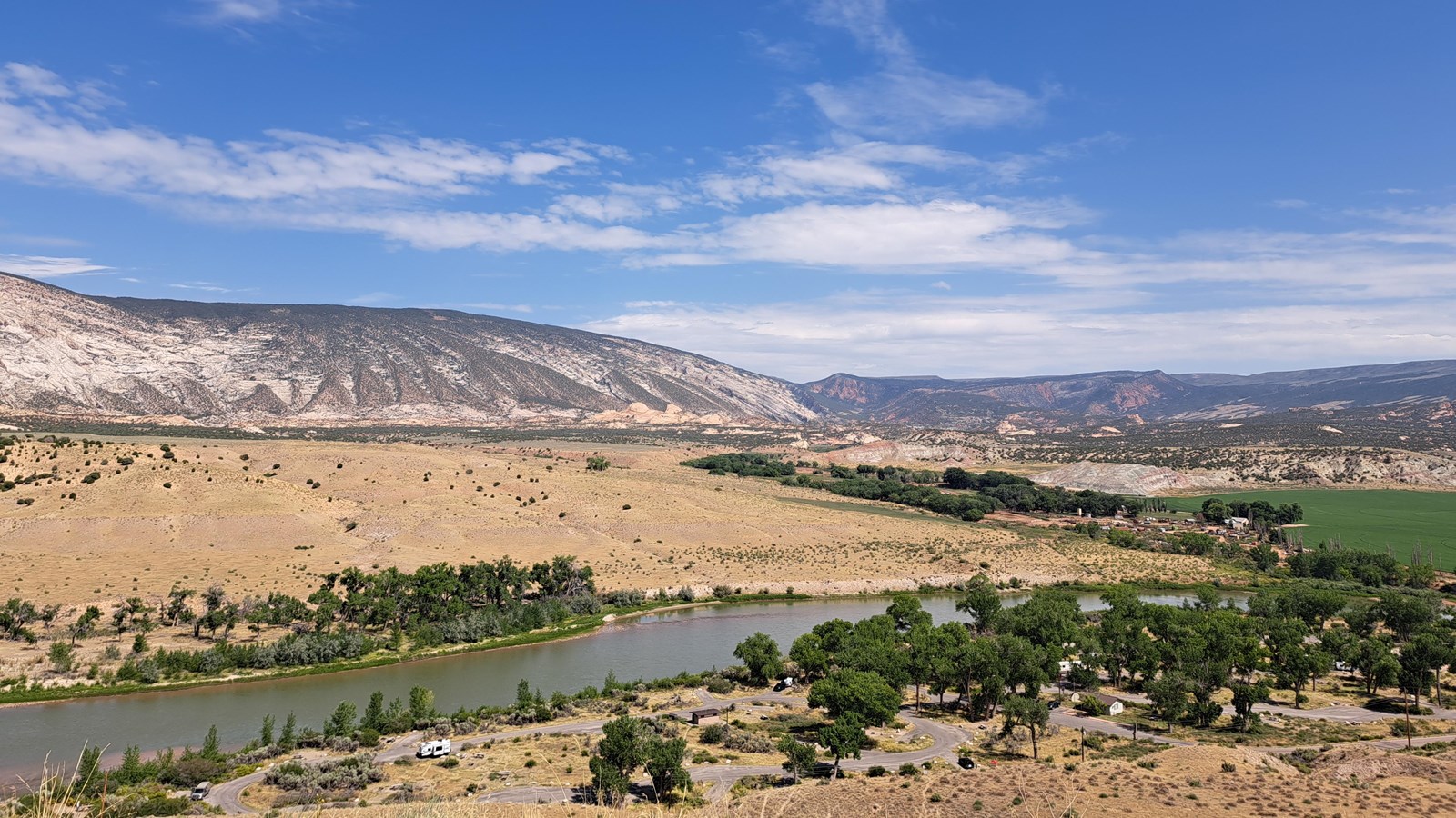 A panoramic view from a roadside pullout overlooking a vast valley between two desert mountains.