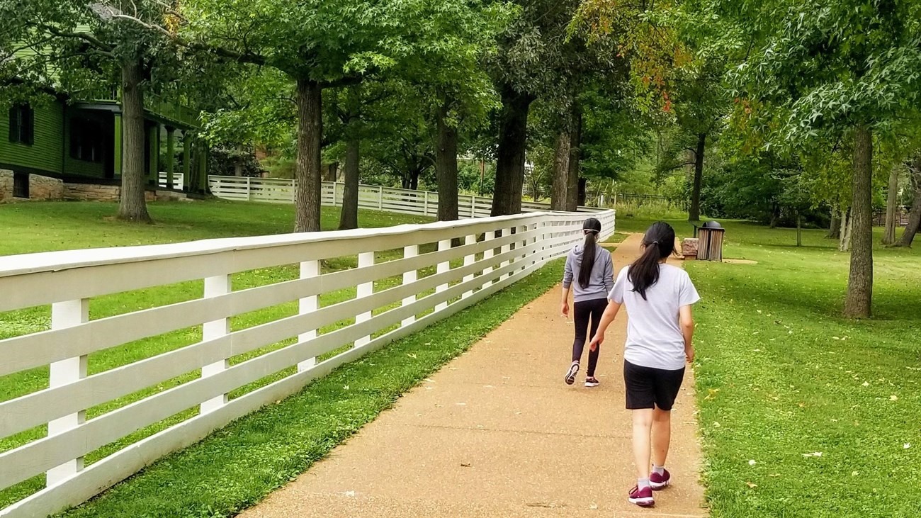 Two women walking on a stone path surrounded by trees