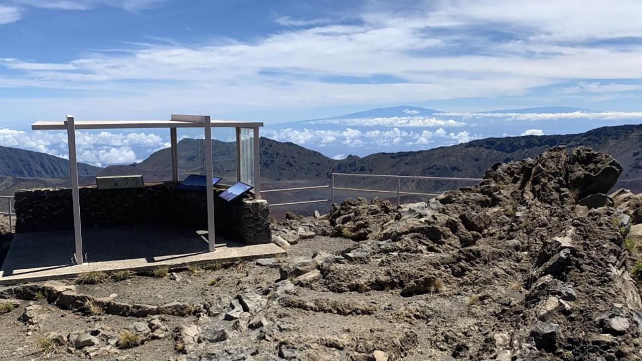 Rocky overlook area with a simple metal and glass structure on the edge of the crater.