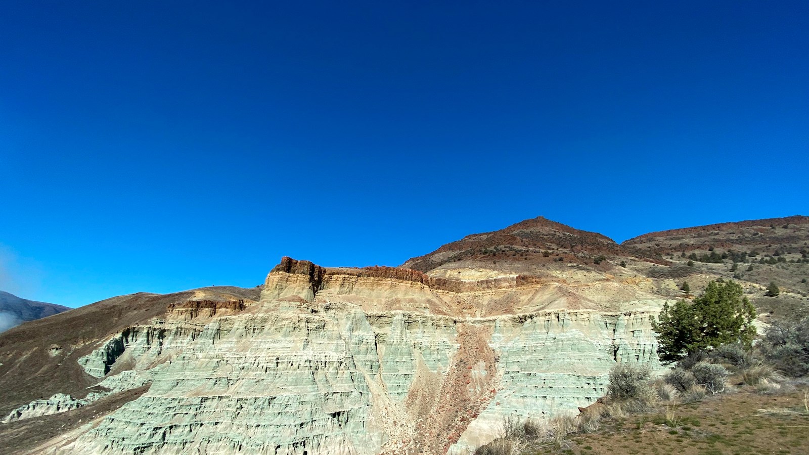 Blue-green rock formation with thin red rock layer on top.