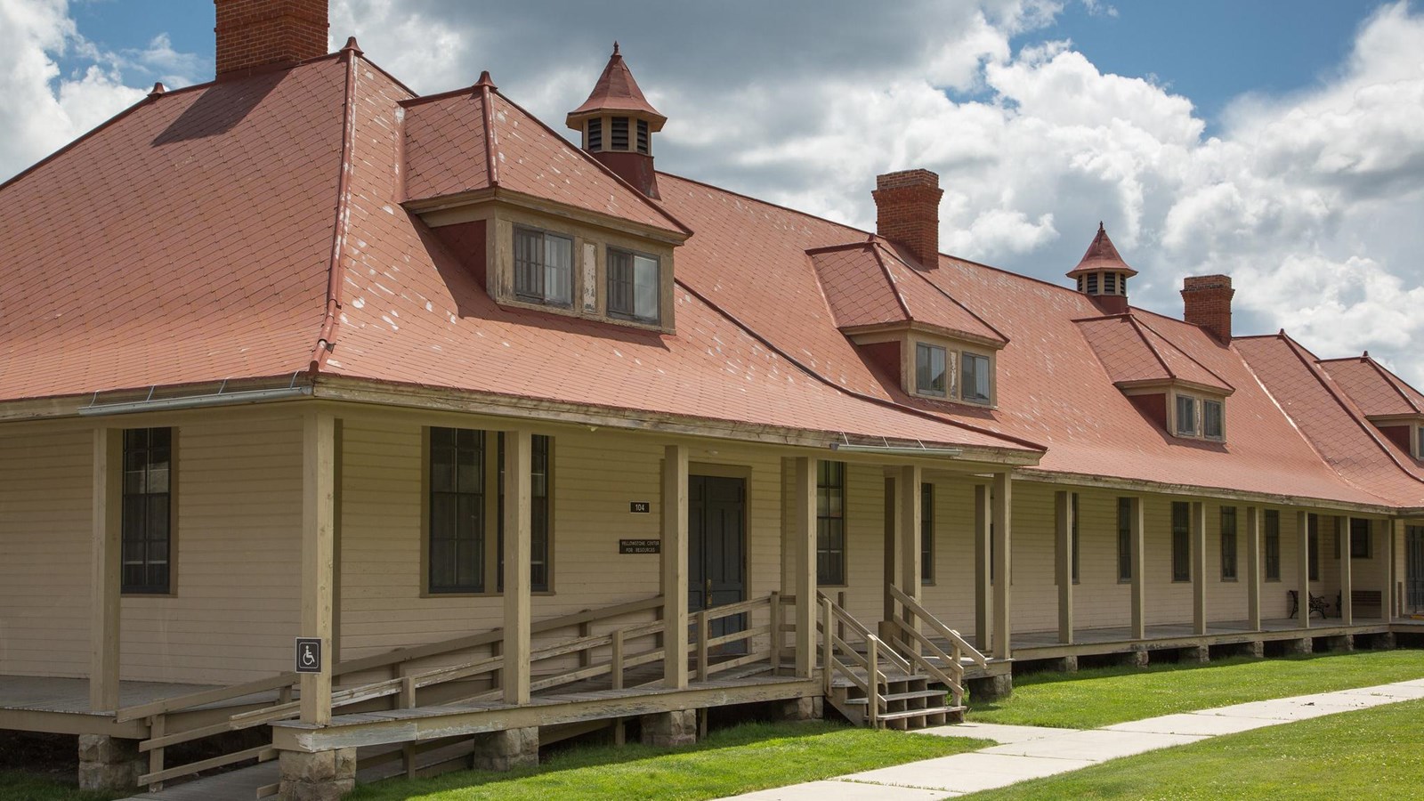 A historic building with pale yellow siding and a roof with red shingles.