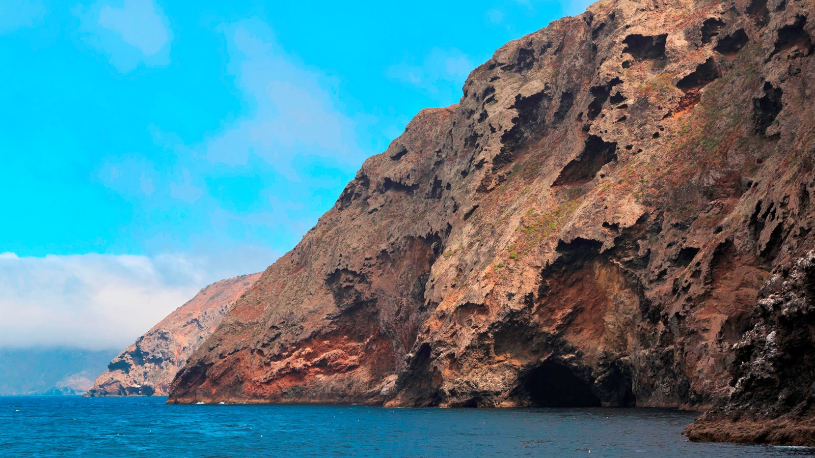 Rugged steep volcanic cliffs with blue ocean.