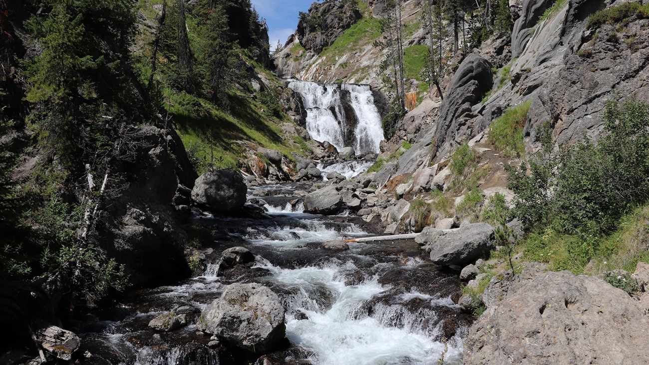 A waterfall cascades over a cliff and flows into a stream down a rocky creek.