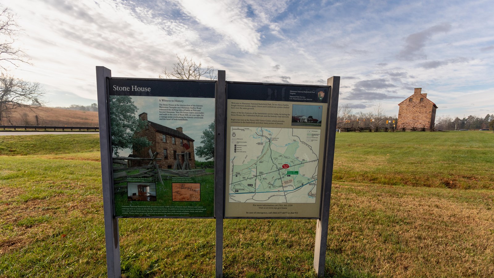 Two information panels in front of a grassy field with a house in the distance.