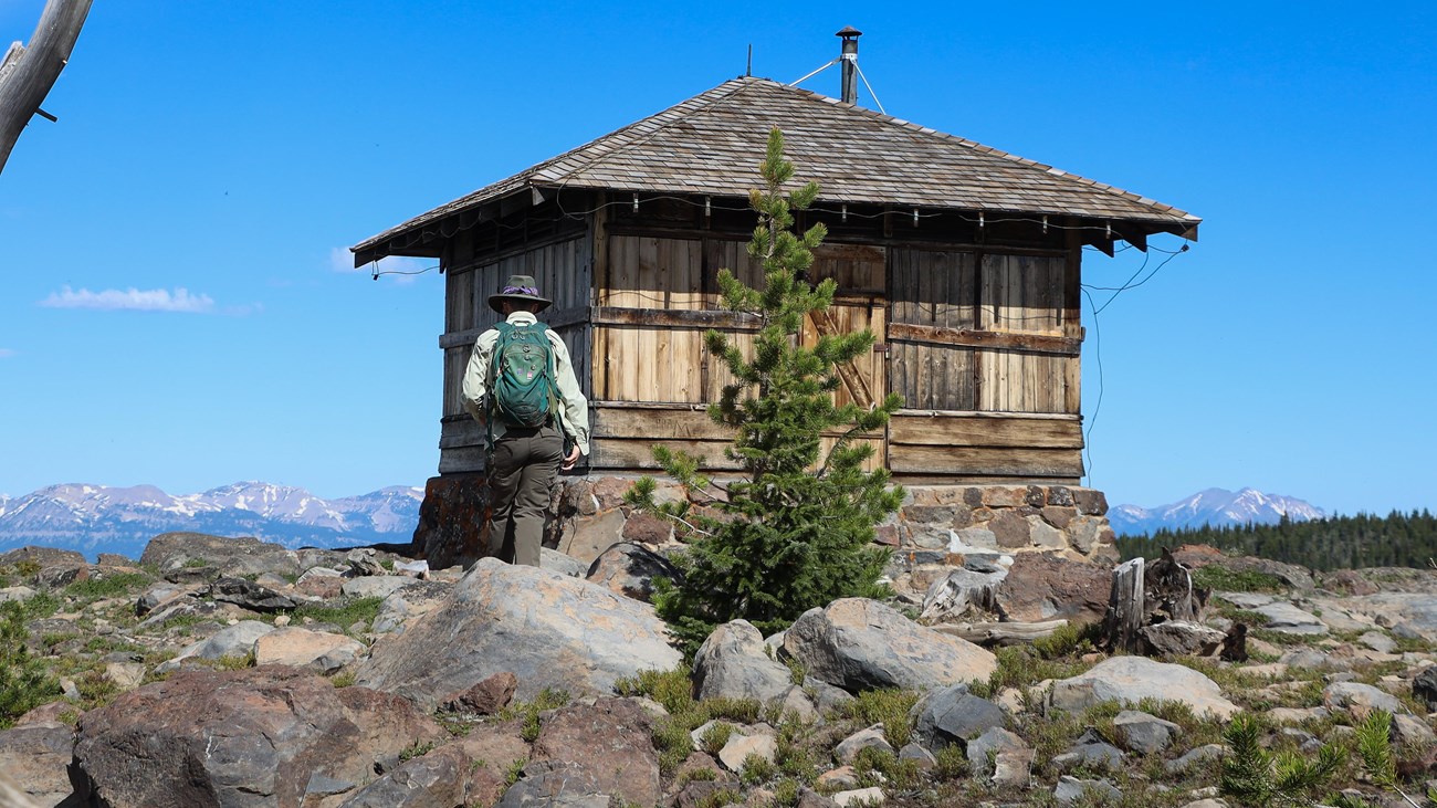 A hiker approaches a fire lookout on top of a mountain.