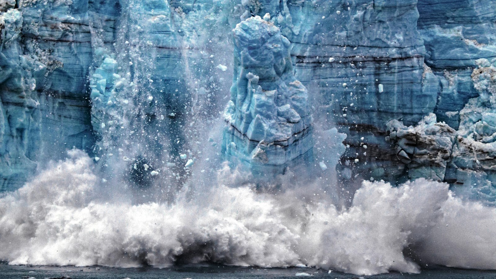 Crumbling glacial ice fills the scene. A torrent of crumbling ice is captured splashing into water.