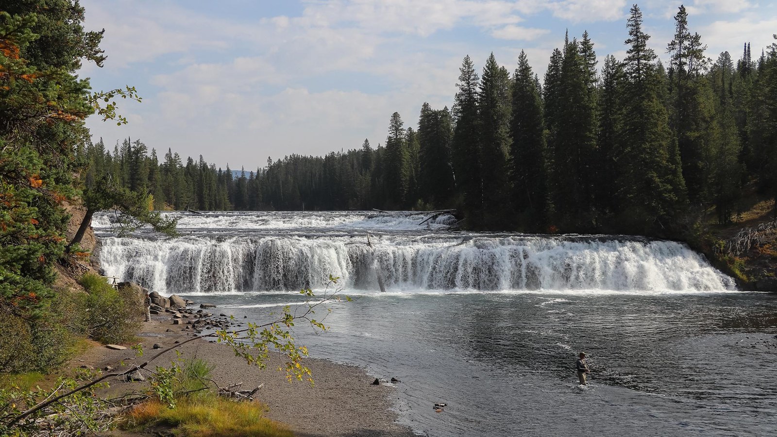 A waterfall cuts across a broad river.