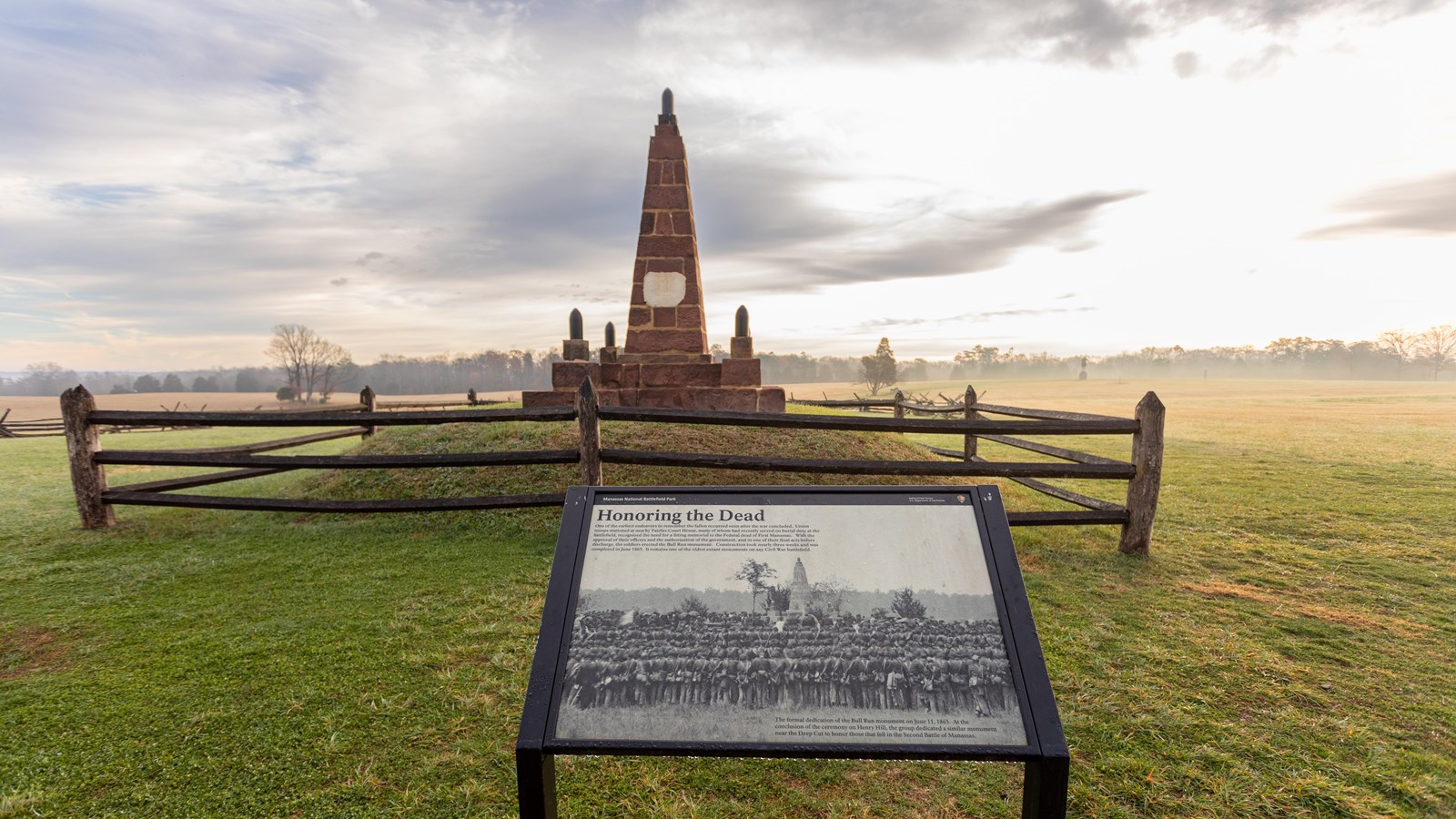 An informational panel in front of a monument in a grassy field.